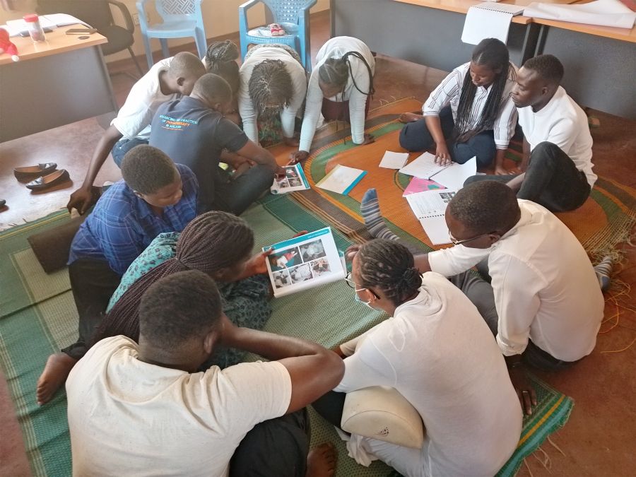 A group of Baby Ubuntu training participants sit in groups on the floor. Each group looks over a book, examining the training material together. 